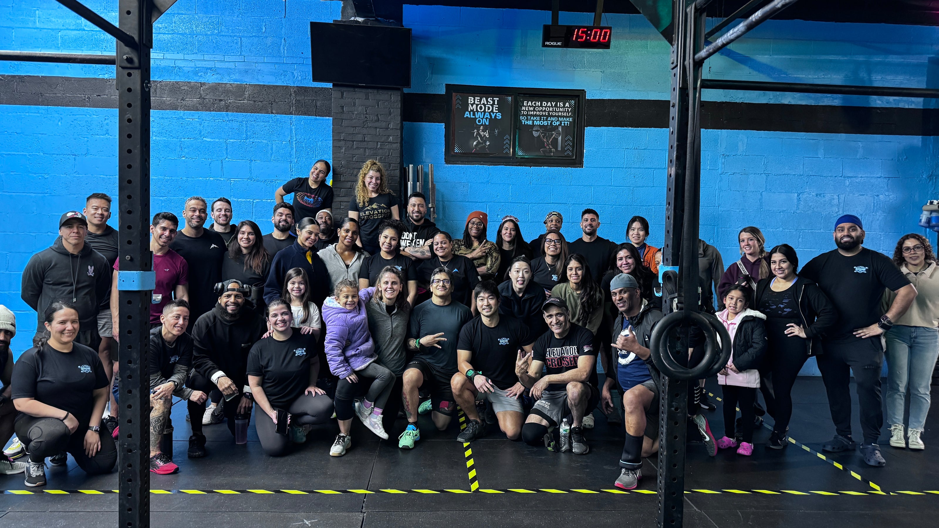 Group of people posing for a photo in a gym with blue walls and weightlifting equipment.